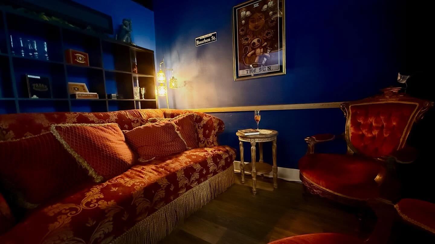 The Bourbon Street Parlor at Elixir VI, with a red patterned sofa, velvet armchairs, and warm lantern light against navy walls