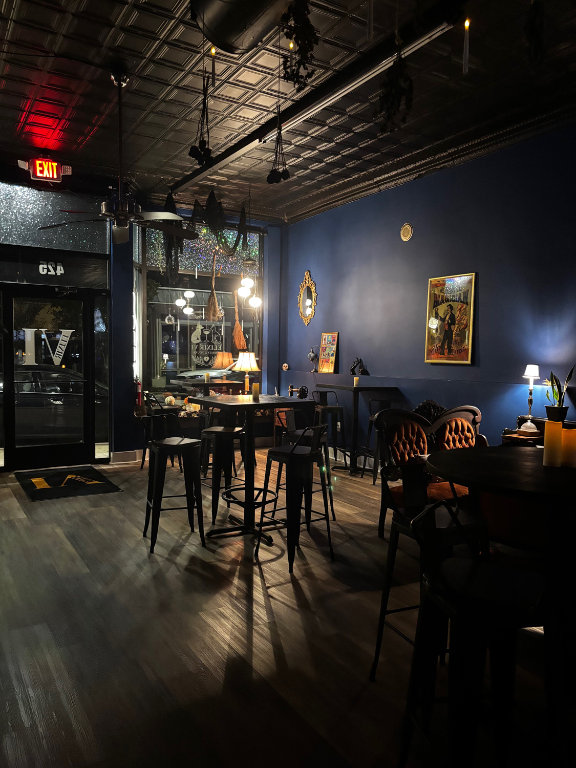 Elixir VI's intimate interior with navy walls, candlelit tables, velvet seating, and an ornate tin ceiling